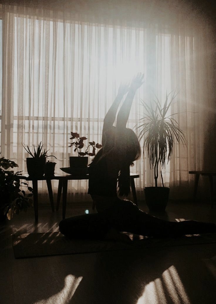 A figure stretching by a window among houseplants
